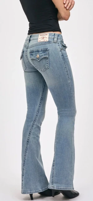 True Religion jeans - Snygga ljusblå jeans från True Religion med klassiska fickor och dekorativa sömmar bak. Modellen har låg midja och bootcut-ben som ger en schysst siluett. Jeansen är tillverkade i mjukt denim och har knappar och dragkedja framtill.                                                     Jag har sytt om jeansen hos en skräddare, så de passar mig som är 160cm!