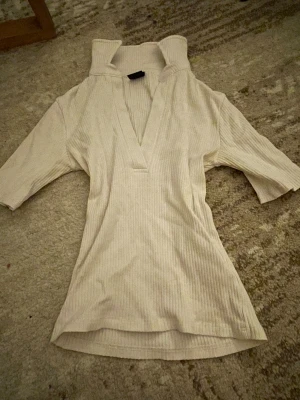 Vit ribbad polotopp från Gina Tricot - Säljer en vit ribbad polotopp från Gina Tricot i storlek XS. Toppen har en hög krage, v-ringad öppning framtill och halvlånga ärmar. Materialet är mjukt och stretchigt, perfekt för att ge en snygg och slim passform. Enkel och clean look som funkar till många stilar.