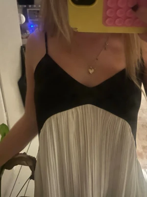 Svart och vit plisserad linnetopp - Säljer en snygg linnetopp med smala axelband och v-ringning. Toppen är svart upptill och har en vit, plisserad nederdel som ger en cool kontrast och flowig känsla. Perfekt för dig som gillar stilrena och trendiga plagg med lite extra volym. Är 160 och den är för stor i ryggen tyvärr men så sjukt snygg! 