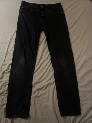 Svarta jeans från Kappahl, storlek 170 - Svarta jeans från Kappahl i storlek 170. Klassisk femficksmodell med dragkedja och knapp framtill. Jeansen har en rak passform och är tillverkade i mjukt denimtyg som sitter skönt hela dagen.