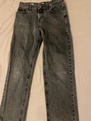 Grå jeans från Jack & Jones - Säljer ett par grå jeans från Jack & Jones med klassisk femficksdesign och raka ben. Jeansen har en snygg tvättad look och svarta detaljer vid sömmarna. Passar dig som gillar enkel och stilren denim med lite edge.