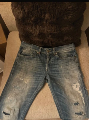 Dondup George  - Säljer ett par blå skinny jeans från DonDup med slitna detaljer och hål på benen för en cool, edgy look. Jeansen har klassisk femficksdesign, knapp och dragkedja i midjan samt skinny fit som sitter tajt längs benen. Perfekt för dig som gillar streetstyle.