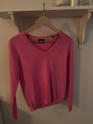 Rosa v-ringad tröja från GANT - Snygg rosa tröja från GANT med v-ringad hals och lång ärm. Diskret logga broderad på bröstet. Mjuk och tunn kvalitet i bomull, perfekt för dig som gillar klassisk stil med färg. Passar dig som vill ha en enkel men stilren look. Tveka inte att skriva om du har några funderingar elelr vill ha fler bilder❤️(Är M men passar S likadant)