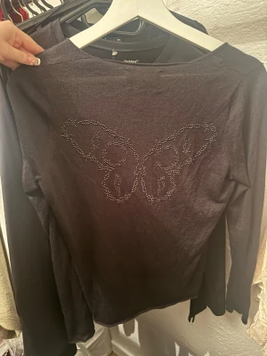 Svart v-ringad tröja Zadig & Voltaire - Svart långärmad tröja från Zadig & Voltaire med v-ringning och ett snyggt fjärilsmotiv i pärlor på ryggen. Mjuk och tunn kvalitet, perfekt för dig som gillar stilrena detaljer med lite edge. Passar dig som vill ha en enkel men cool look.