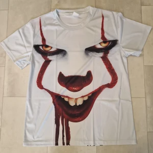 Vit t-shirt med Pennywise tryck - Säljer en vit t-shirt med ett stort, detaljerat tryck av Pennywise från filmen IT på både fram- och baksidan. T-shirten har korta ärmar och är tillverkad i ett mjukt syntetmaterial som känns skönt mot huden. Perfekt för dig som gillar skräck och vill sticka ut.