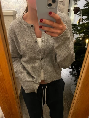 Grå kofta från Lindex  - Mysig grå kofta från Lindex i storlek S. Den har rund hals, långa ärmar och knappar framtill. Materialet är mjukt och stickat, perfekt för lager-på-lager. Enkel och clean look som funkar till många olika stilar.