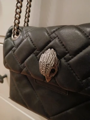 Svart quiltad axelväska Kurt Geiger - Snygg svart quiltad axelväska från Kurt Geiger med kedjerem och ikoniskt ugglehuvud i silver som låsdetalj. Väskan är i skinn och har en stilren, boxig form som ger en lyxig känsla. Perfekt för dig som vill ha något trendigt och unikt.