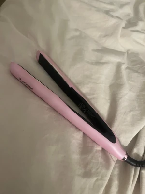 Rosa plattång från HH Simonsen - Snygg plattång i ljusrosa färg från HH Simonsen med svarta keramiska plattor och sladd. Perfekt för att styla håret och skapa både raka och vågiga looks. Ergonomisk design och lätt att använda. Passar dig som vill ha ett trendigt verktyg i sminkväskan. Nypris 2595