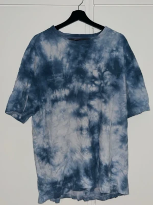 Blå tie-dye t-shirt i bomull - Säljer en blå och vit tie-dye t-shirt med avslappnad passform. T-shirten har korta ärmar och är gjord i bomull. Använd ett flertal gång och är skön att sova i. Från Lager157