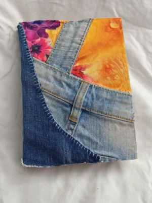 Handgjord anteckningsbok med jeansomslag - Unik anteckningsbok med omslag av återvunna jeans och färgglada tygdetaljer. Perfekt för dig som vill sticka ut och skapa egna berättelser, teckningar eller dagboksanteckningar. Grovt papper ger en kreativ känsla och jeansfickan på baksidan är perfekt för småsaker. A5 storlek ca 50 sidor