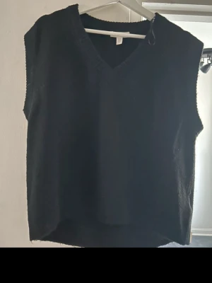 Svart stickad väst från H&M - Svart stickad väst från H&M i storlek XS. Västen har v-ringad hals och är enkel i designen utan mönster eller detaljer. Perfekt att slänga över en skjorta eller t-shirt för en chill och stilren look.