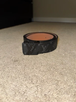 Exklusivt svart monogrambälte - Riktigt snyggt svart bälte med elegant monogrammönster och stilrent svart metallspänne med ikonisk bokstavsdesign. Perfekt accessoar som lyfter vilken outfit som helst – funkar lika bra till jeans som till mer uppklädd stil. Bältet är i mycket fint skick och ger ett lyxigt, modernt intryck. Ett måste i garderoben!