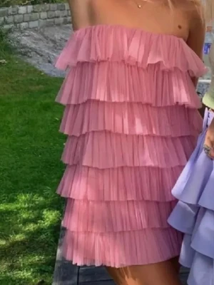Rosa volangklänning med axelbandslös design - Supersöt rosa kortklänning med flera lager volanger och axelbandslös design. Klänningen har tunna axelband som kan knytas🩷