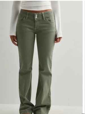 Gröna bootcut jeans med broderi - Snygga gröna jeans med bootcut-snitt och klassisk femficksdesign. Byxorna har två knappar i midjan och dekorativa broderade detaljer på bakfickorna. Materialet är jeans och passformen är normal med något utsvängda ben.