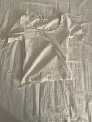 Vit kortärmad t-shirt med rund hals - Säljer en enkel och fräsch vit t-shirt med rundad halsringning och korta ärmar. Modellen är rak och klassisk, perfekt att matcha med jeans eller shorts. Materialet känns mjukt och lätt, troligtvis bomull. En basic tee som alltid funkar.