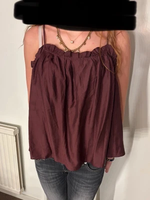 Vinröd ärmlös linnetopp med volang - Säljer en vinröd, luftig linnetopp med volangkant och smala axelband. Toppen har en öppen rygg med knytband och ett avslappnat, loose fit. Aldrig andvend 