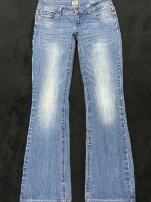 Bootcut jeans från ONLY, blå - Bootcut jeans från ONLY i ljusblå tvätt med slitningar och klassiska fem fickor. Jeansen har låg midja, bälteshällor och dragkedja med knapp. Materialet är mjukt denim i bomull och passformen är loose med breda ben. Perfekt för dig som gillar retrovibbar och avslappnad stil.