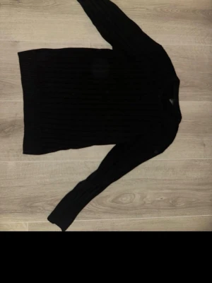 Svart ribbad stickad tröja - Säljer en svart stickad tröja med ribbad struktur. Tröjan har långärmade och en klassisk rund halsringning. Perfekt för dig som gillar enkla och stilrena plagg med lite edge. Passar till jeans eller kjol för en chill look.