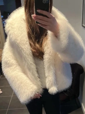 Vit fluffig pälsjacka - Säljer en supermjuk och fluffig vit pälsjacka med bred krage och långärmad design. Jackan har en oversized passform och är perfekt för dig som vill ha en statement piece i garderoben. Passar dig som gillar att sticka ut och hålla dig varm. Använt ett fåtal gånger, inga defekter. Lånad bild