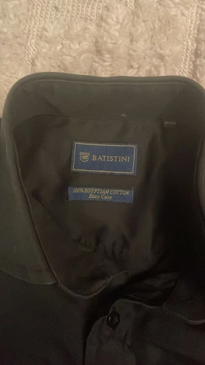 SVART BATISTINI SKJORTA 100% EGYPTIAN COTTON - Svart Batistini skjorta. 100% Egyptisk Bomull. Är ju troligtvis några år gammal då jag fick den av farsan men fortfarande otroligt fin. Om den inte var så gammal som den är hade jag satt nytt skick. Inga defekter. Är 167 och den är lite för lång för mig.