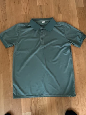 Grön polotopp med krage och knappar - Säljer en stilren grön polotopp i polyester med klassisk krage och tre knappar framtill. Toppen har korta ärmar och en slät, enkel design som passar perfekt till jeans eller shorts. Perfekt för dig som gillar en clean och sportig look.