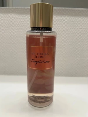 Victoria's Secret Temptation Mist - Fragrance mist från Victoria's Secret i varianten Temptation. Flaskan rymmer 250 ml (8.4 fl oz) och har en stilren design med guldfärgat lock. Perfekt för dig som vill ha en lätt och fräsch mist i din samling.