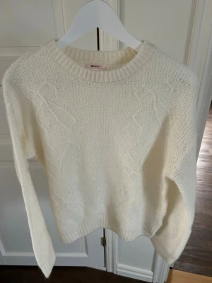 Vit stickad tröja från Gina Tricot - Mysig vit stickad tröja från Gina Tricot med  rosettdetaljer på framsida och baksida. Aldrig använd. Köpt på Young avdelningen så storleken är S 14+