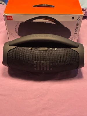 JBL Boombox 3 högtalare - JBL Boombox 3 bärbar Bluetooth-högtalare i svart, med kraftfullt ljud och robust design. Utrustad med USB-C, USB-A och AUX-port. Produkten ser ut att vara i mycket gott skick utan synligt slitage. Perfekt för både inomhus- och utomhusbruk.