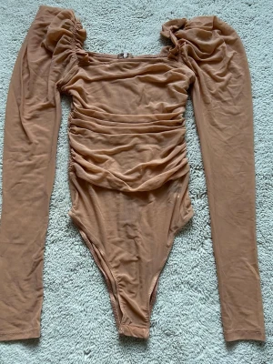Beige långärmad bodysuit från SHEIN - Säljer en beige bodysuit från SHEIN med puffiga långärmade ärmar och snygg rynkad detalj framtill och baktill. Den är använd endast en gång🌸