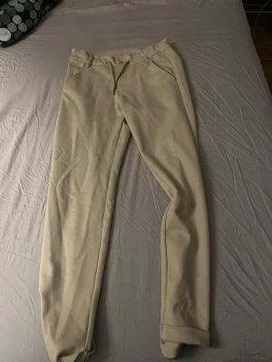 Beige chinos från Kappahl - Snygga beige chinos från Kappahl i storlek 146. Byxorna har klassisk passform med snörning i midjan, bälteshällor och fickor fram och bak. Materialet är mjukt och bekvämt, perfekt för en chill och stilren look.