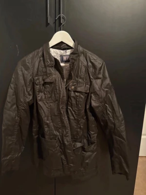 Brun skinnjacka från Jofama, strl 36 - Snygg brun skinnjacka från Jofama med coola detaljer som fickor med knappar och ståkrage. Jackan har långärmade ärmar och ett blommigt innerfoder i grått och vitt. Perfekt för dig som vill ha en stilren och edgy look.