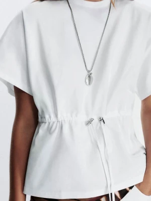 Vit topp med snörning i midjan - Säljer en vit topp med korta ärmar och rund hals. Toppen har en snygg snörning i midjan som ger en cool och modern siluett. Materialet är mjukt och känns skönt mot huden, perfekt för varma dagar. Enkel och stilren design som funkar till många olika looks.