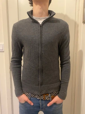 Grå merinoullskofta från These Glory Days - Säljer en stilren grå kofta i mjuk merinoull från These Glory Days. Koftan har hel dragkedja framtill, hög krage och lång ärm. Perfekt för lager-på-lager och funkar året runt. Enkel och clean design som passar till det mesta.storlek XS pris kan diskuteras. Nypris 1199
