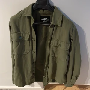 Olivgrön overshirt från Mads Nørgaard - Olivgrön overshirt från Mads Nørgaard med klassisk krage, skönt plagg. Perfekt lager-på-lager-plagg för en chill look. Pris kan diskuteras vid snabbt köp.