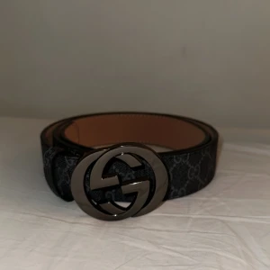Svart bälte  - Säljer ett stilrent svart bälte med klassisk rund metallspänne i mörk silver. Bältet har det ikoniska GG-mönstret och är tillverkat i skinn med insida i beige. Perfekt accessoar för att lyfta din outfit. Kommer även med box och påse😀