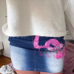 Jeanskjol  - Cool jeanskjol från Fishbone i klassisk blå denim med blekta partier och färgstark graffiti-inspirerad text och rosa detaljer fram och bak. Kjolen har fem fickor, bälteshällor och knapp med fiskbensdetalj. Perfekt för dig som vill sticka ut med en edgy streetstyle.