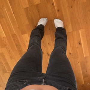 Svarta bootcut jeans med hål - Säljer ett par svarta bootcut jeans med klassisk femficksdesign och dragkedja. Jeansen har en snygg passform med lite utsvängda ben och ett hål på bakfickan för en extra edge. Perfekta till sneakers eller boots.