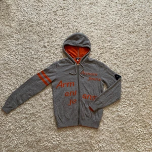 Grå stickad hoodie från Armani Jeans - Sjukt snygg stickad hoodie från Armani. Den är grå med orangea detaljer och orange på insidan, väldigt unik har inte sett denna hoodien någon annan stans. Den är sjukt skön och bekväm och i gott skick. Står strl L men passar mig perfekt som brukar bära M! Tveka inte o skriva vid frågor!