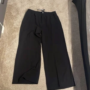 Svarta vida kostymbyxor - Svarta kostymbyxor med breda ben och hög midja. Byxorna har en klassisk och stilren look med diskret dragkedja i sidan. Perfekta för dig som gillar en loose och relaxed passform. Materialet känns mjukt och följsamt. Helt nya från weekday, 670 kronor nypris