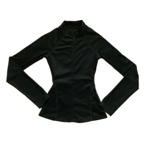 Svart långärmad polotröja - Slimmad svart polotröja med lång ärm och hög krage. Tröjan har en diskret half zip-dragkedja framtill och markerade sömmar som ger en snygg siluett. Perfekt för lager-på-lager och stilrena outfits.