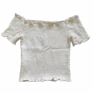 Vit offshoulder smockad topp - Liten i storleken uppskattar till en XS/S Söt vit topp med smockad struktur och offshoulder-modell. Toppen har korta ärmar med volangkant och vågig nederkant för en extra gullig touch. Perfekt för dig som gillar en feminin och trendig stil.