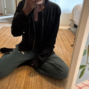 Svart bomberjacka med rosa foder - Säljer en svart bomberjacka från H&M med snyggt rosa foder. Jackan har guldiga dragkedjor, ribbade muddar och klassisk bomberkrage. Materialet är polyester och jackan har fickor med tryckknapp samt ärmlängd som går till handleden.