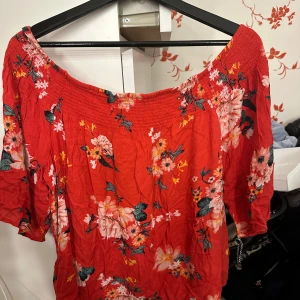 Röd blommig offshoulder-top Gina Tricot - Säljer en röd blommig offshoulder-top från Gina Tricot i storlek 44. Toppen har bred resår upptill, korta ärmar och ett färgstarkt blommönster i rosa, vitt och grönt. Perfekt för dig som gillar en luftig och somrig stil.