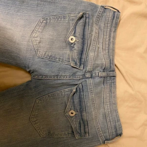 Ljusblå lågmidjade bootcut jeans - Säljer ett par ljusblå bootcut jeans med klassiska femficksdetaljer och knappstängning. Jeansen har en snygg tvätt och är perfekta för en avslappnad stil. 82cm i midjan och längden är 100cm❤️