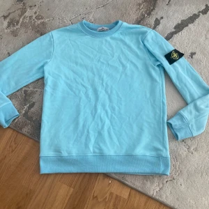 Ljusblå Stone Island sweatshirt M - Säljer en ljusblå sweatshirt från Stone Island med klassisk patch på ärmen. Tröjan har rund hals, ribbade muddar och är tillverkad i mjuk bomull. Perfekt för dig som gillar streetwear och vill sticka ut med en clean look.
