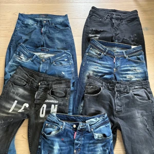 Dsquared2 jeans i olika tvättar - Flera par Dsquared2 jeans säljes, både svarta och blå tvättar med slitningar, färgstänk och tryckdetaljer. Några har stora loggor och dragkedjor, alla med klassisk femficksdesign och snygga Dsquared2-lappar bak. Perfekta för dig som gillar streetwear och statement-plagg.
