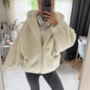 Oversized teddyjacka med huva - Mysig oversized teddyjacka med stor huva och dragkedja framtill. Jackan har två fickor på sidorna och är tillverkad i fluffigt teddy-material som ger en chill och trendig vibe. Perfekt för lager-på-lager och att hålla sig varm under kyliga dagar.