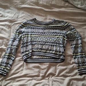 Mönstrad croppad tröja från Divided - Säljer en croppad stickad tröja från Divided med svart, vit och gul zigzag och diamantmönster. Tröjan har långa ärmar och ribbade muddar. Den har även ett hål i ena ärmen som är rätt stort :(