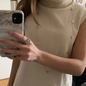 Beige stickad topp från Zara - Säljer en beige stickad väst från Zara med hög, ribbad polokrage. Västen är ärmlös och har en clean, minimalistisk look som är lätt att styla. Perfekt för lager-på-lager och passar till både jeans och kjol.