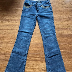 Blå bootcut jeans med guldpaljetter - Blå låga bootcut jeans från Jeans D. med snygga guldpaljetter längs fickorna och broderade bakfickor med texten 'Party Jeans'. Skulle säga att dessa jeans är mer en s/m än en xs/s och är av det lite stretchiga i modellen. Jeansen har en cool och unik look som sticker ut. Säljer då den var för lång för mig som är 161